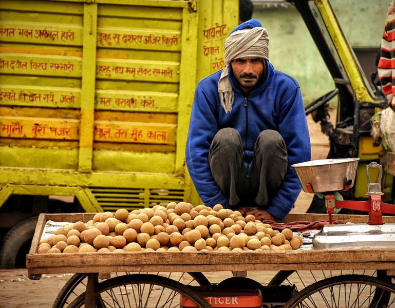 Man in head scarf sitting in front of cart of potatoes.
