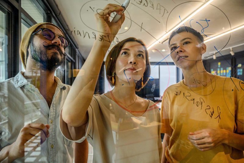 Colleagues writing on a transparent scribble board